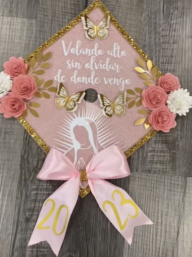 a pink and gold graduation cap with flowers on the front, and a ribbon tied around it