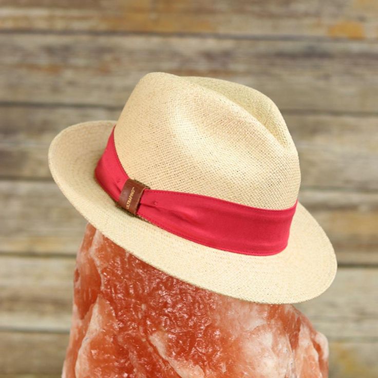 A modern take on the classic fedora Traveler made with 100% toquilla straw and pink or red hatband with leather bow detailing. This effortless piece can easily be worn year-round. The quality can be seen in the beautifully structured crown and stingy brim. This packable fedora is meant for traveling with you wherever you go whether in a suitcase, a purse, or a beach bag. This item is a genuine Panama hat handwoven in Ecuador and blocked and trimmed in the USA. Imported.Crown: 4 1/4" Center DentM Luxury Brimmed Fedora For Vacation, Luxury Fedora With Flat Brim For Vacation, Luxury Fedora Straw Hat For Kentucky Derby, Luxury Flat Brim Fedora For Vacation, Luxury Panama Hat For Spring Vacation, Luxury Travel Hat For Spring, Luxury Spring Travel Hat, Luxury Spring Vacation Panama Hat, Luxury Fedora Panama Hat For Vacation