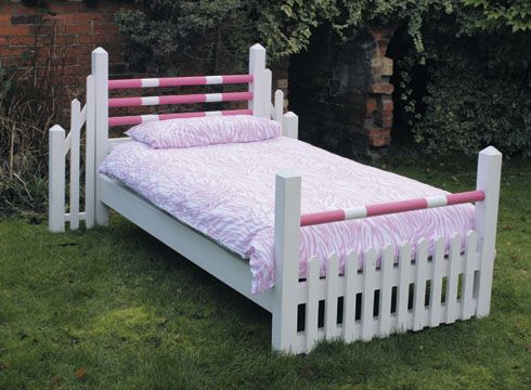 a white bed with pink and white pillows on it in the grass next to a brick wall