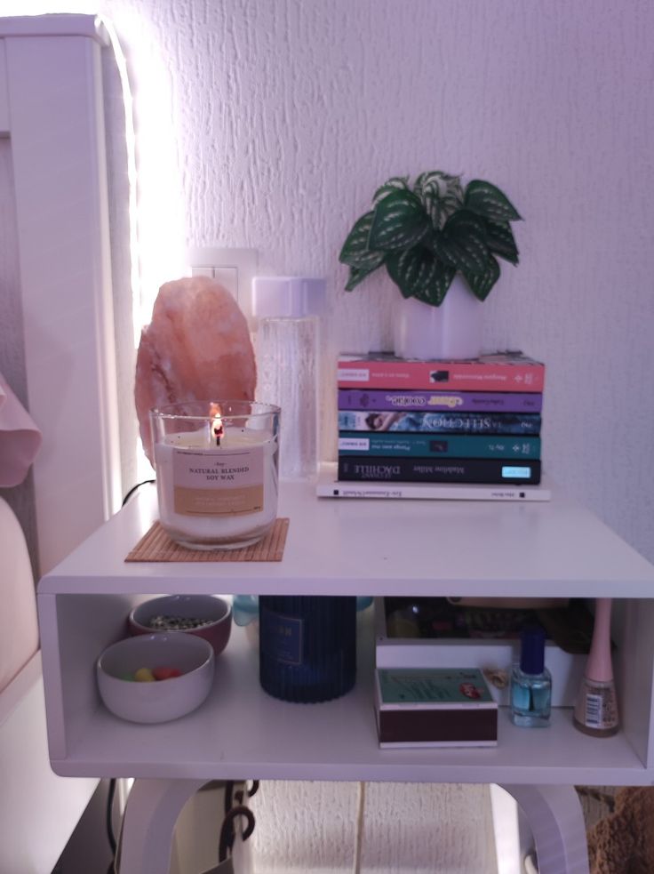 a white table with some books and candles on it next to a potted plant