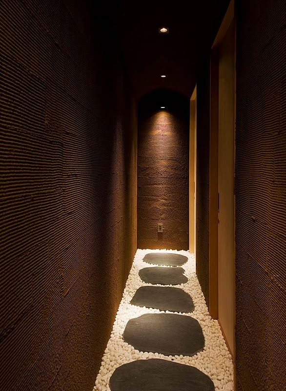 a long narrow hallway with stones on the floor and lights in the wall behind it