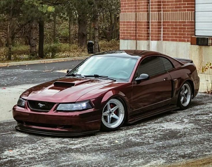 a maroon sports car parked in front of a brick building