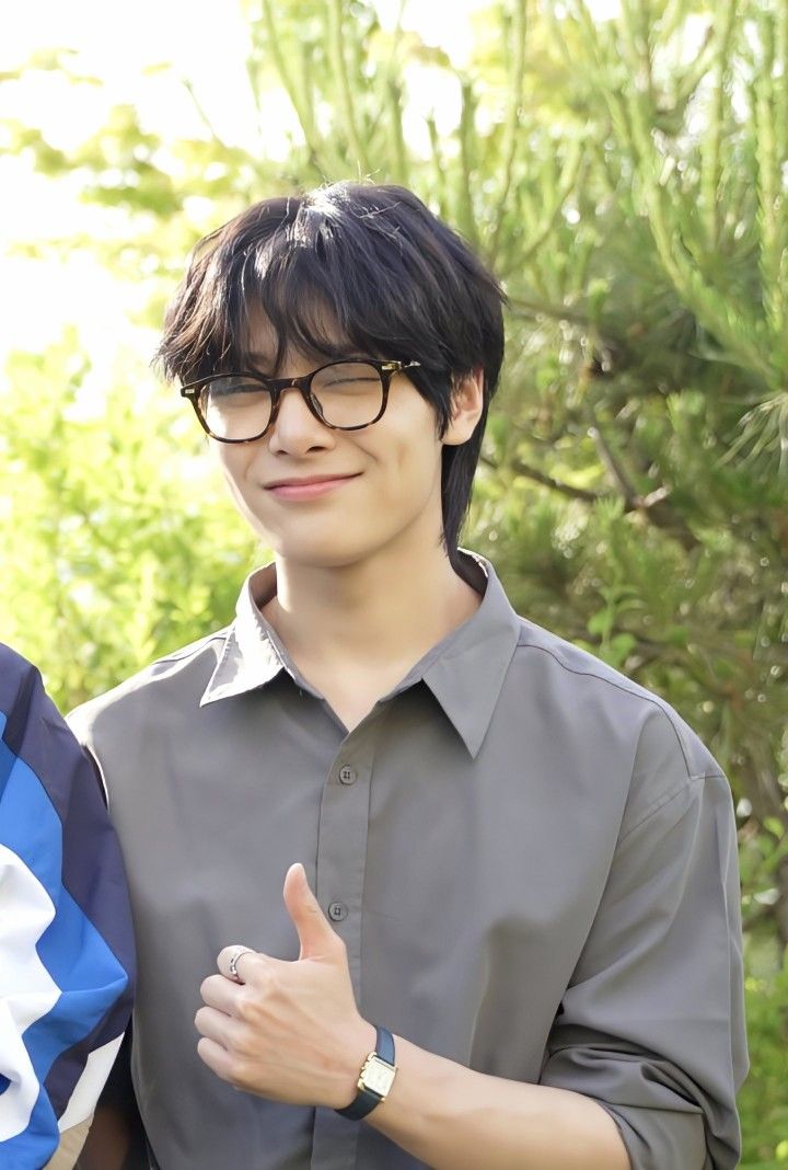 a young man giving the thumbs up sign with another person standing next to him and trees in the background