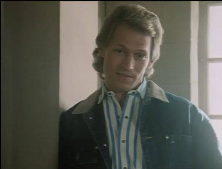 a man standing in front of a window wearing a blue and white shirt with stripes on it