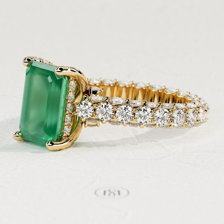 an emerald and diamond ring is shown on a white surface with gold trimmings