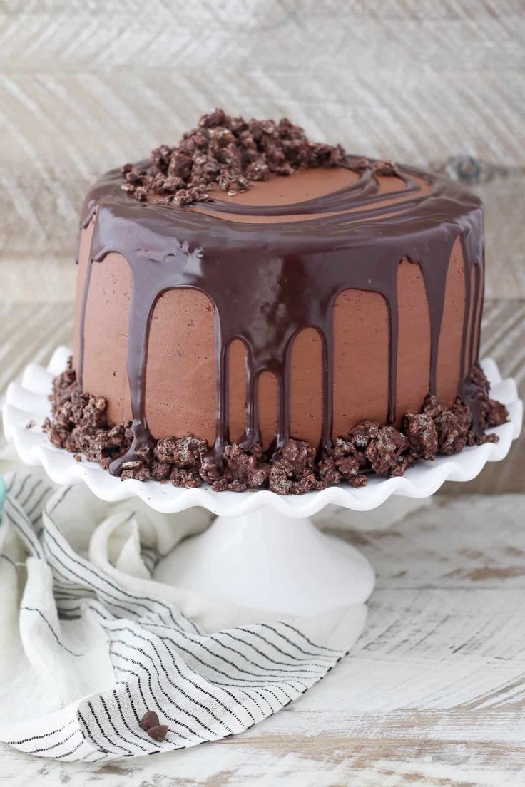 a cake with chocolate icing and chopped cookies on top is sitting on a white plate