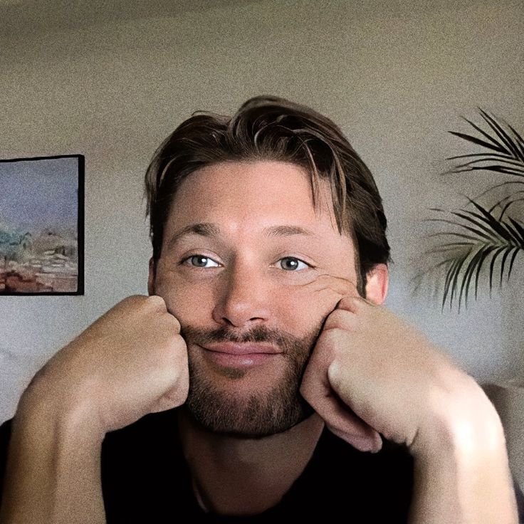 a man sitting in front of a plant with his hands on his face and looking at the camera