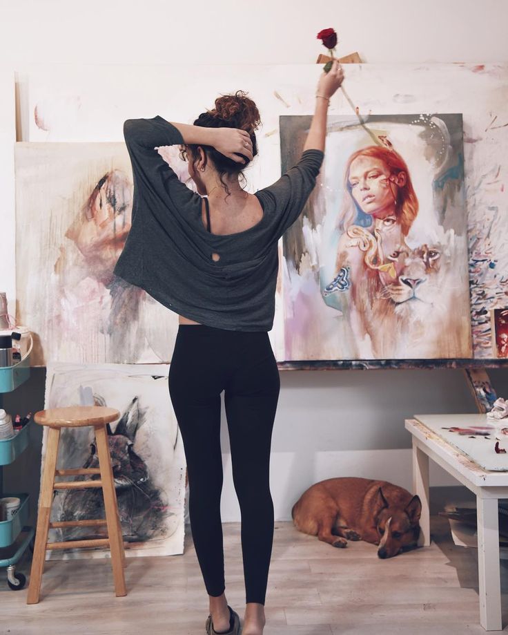 a woman standing in front of an art work holding a rose up to her head