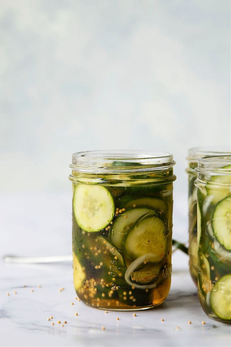 two mason jars filled with pickles and cucumbers on a white counter top