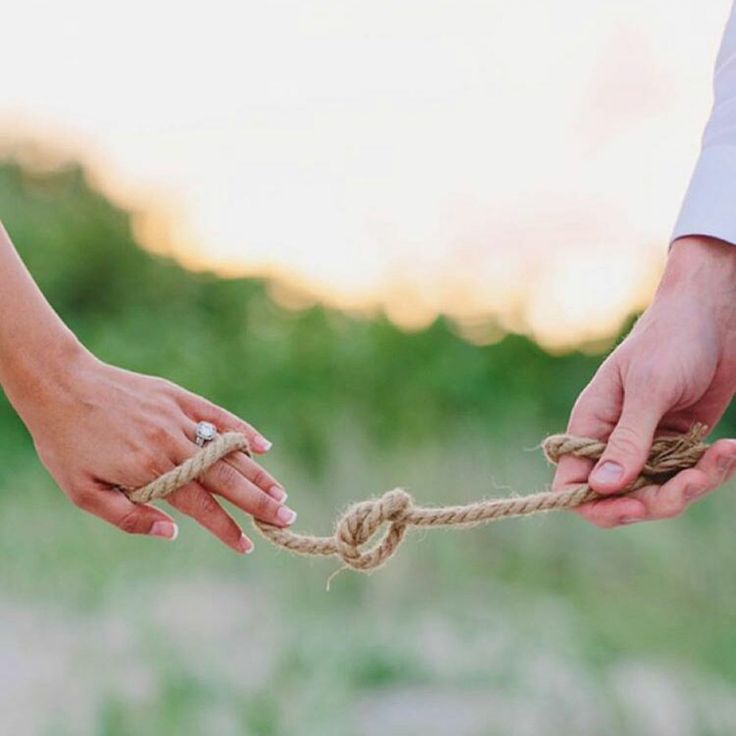 two people holding hands tied up to each other with rope in front of them and grass behind them