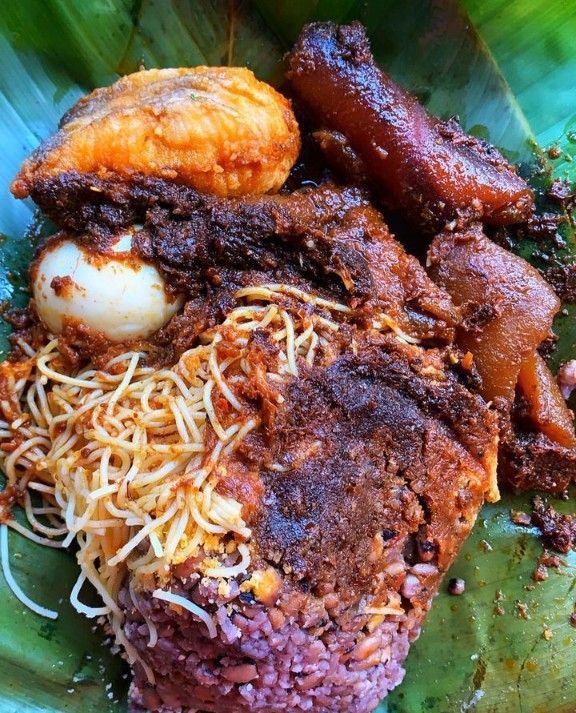 a green plate topped with meat and veggies on top of a banana leaf