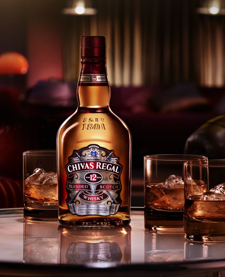 a bottle of chivas regal sitting on top of a table next to two glasses