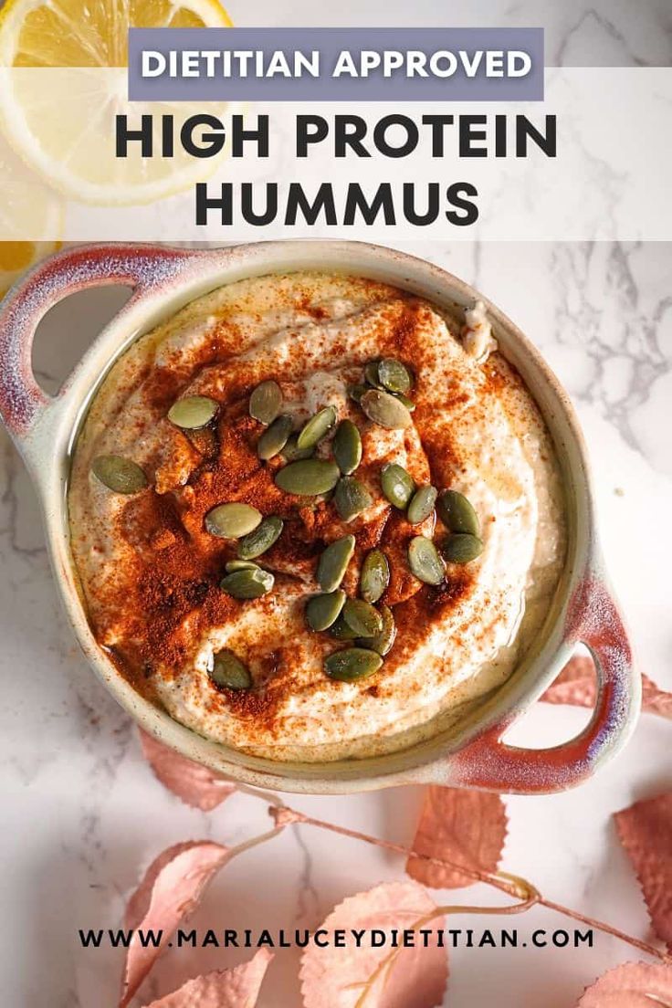 a bowl filled with hummus and topped with pumpkin seeds next to sliced oranges