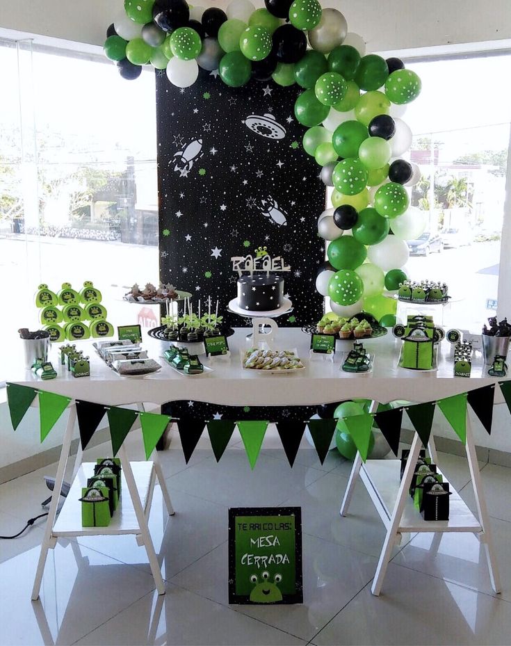 a table topped with green and white desserts next to a space themed cake display