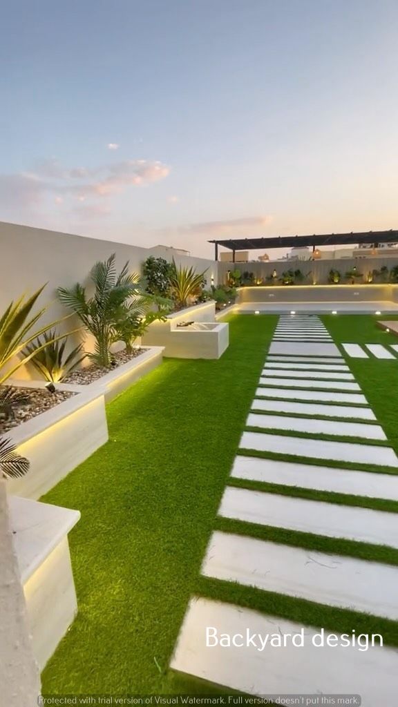 an outdoor garden with grass and white steppings leading to the water feature at dusk