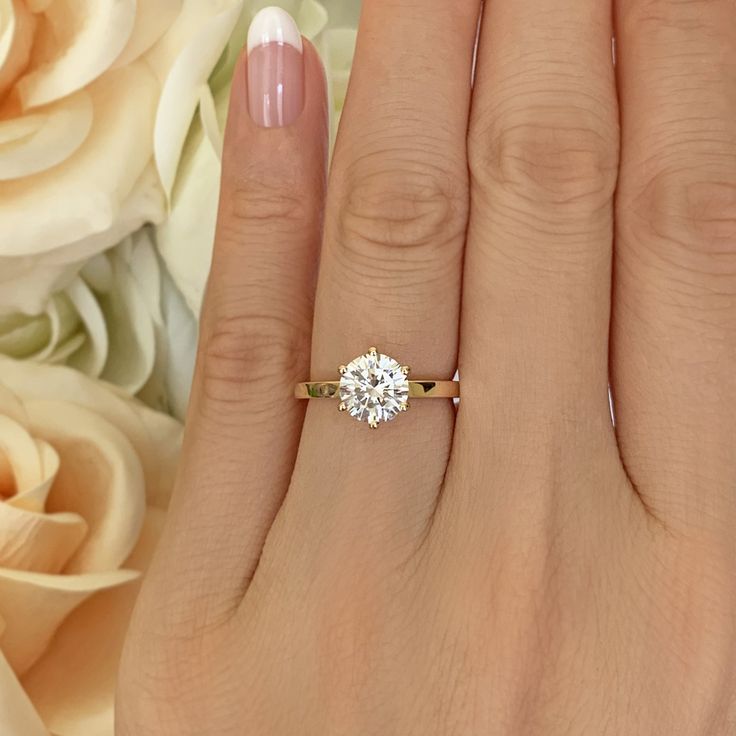 a woman's hand with a diamond ring on it and flowers in the background