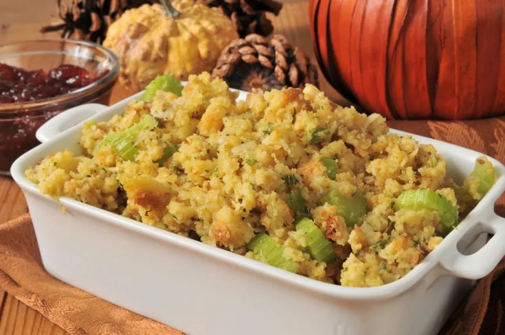 a casserole dish filled with stuffing next to pumpkins and other food items