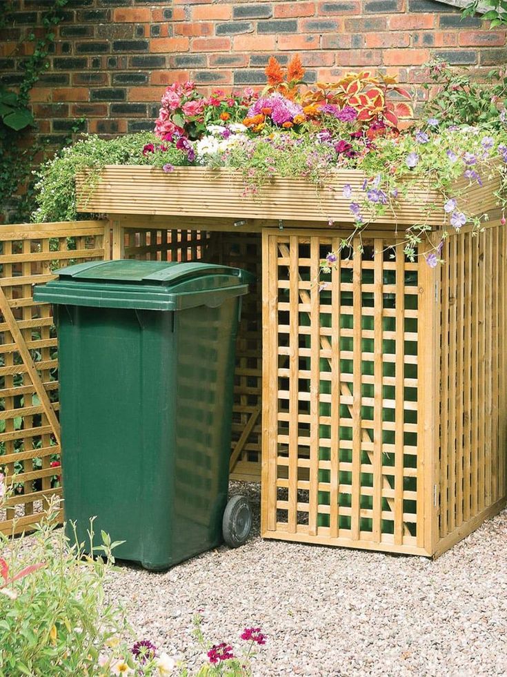 a green trash can sitting next to a wooden table with flowers on it and a plastic bin