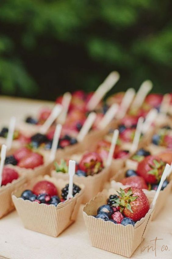 small cups with strawberries and blueberries on them sitting on a table in front of trees