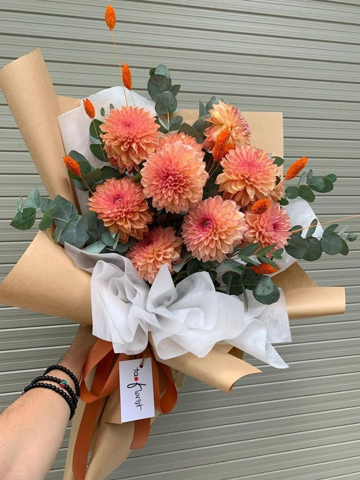 a bouquet of flowers is wrapped in brown paper and being held by someone's hand