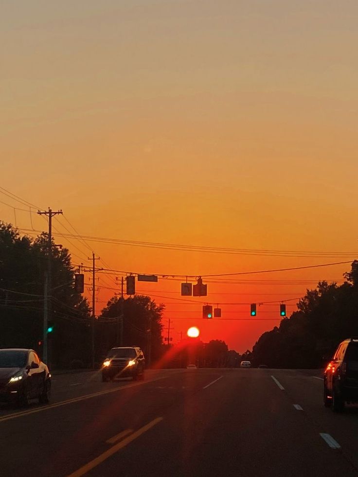 the sun is setting behind some cars on the road