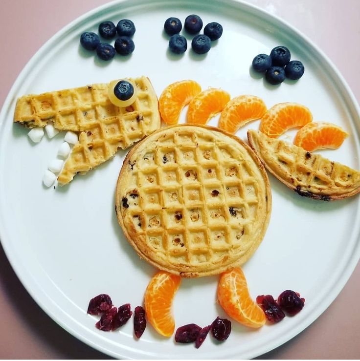 a white plate topped with waffles covered in blueberries and orange wedges