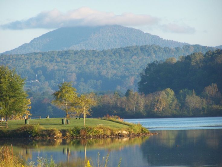 a lake with mountains in the background and people walking on the grass by it,