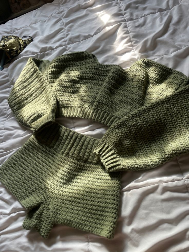 two green knitted sweaters laying on top of a white bed next to each other