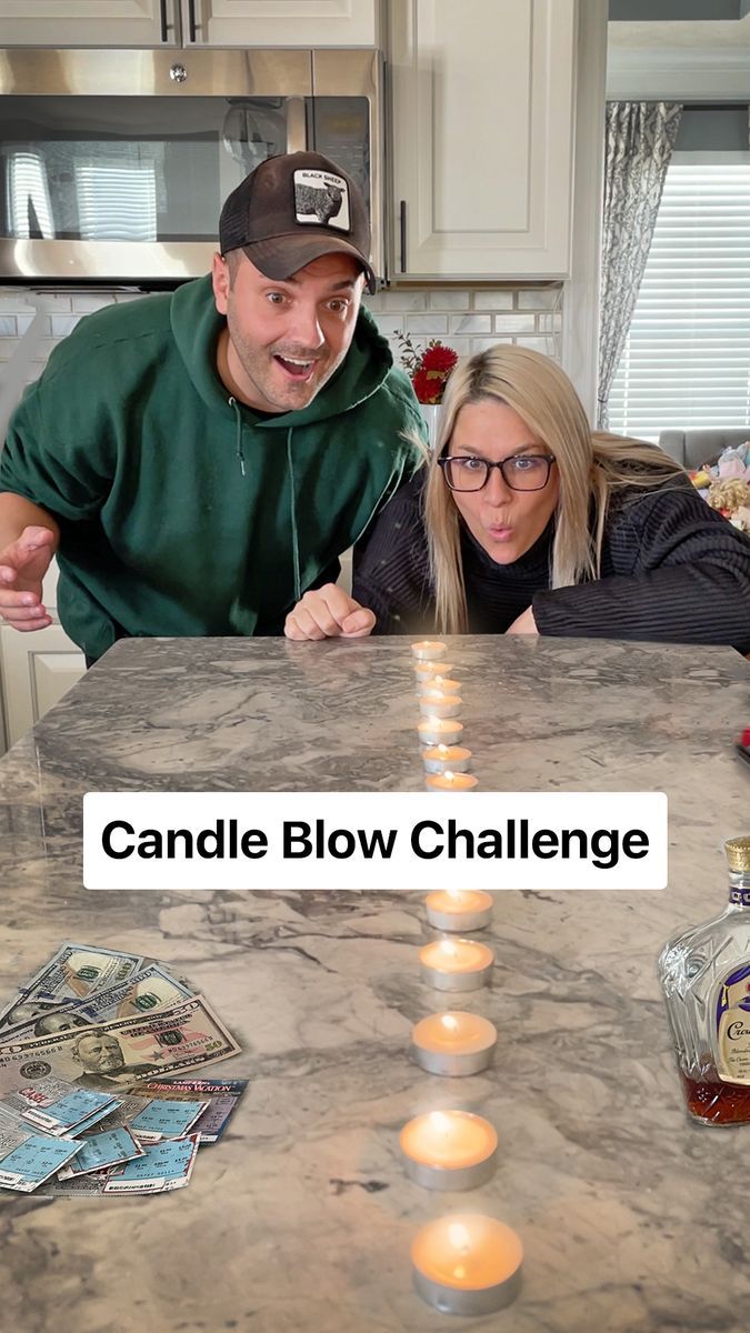 a man and woman sitting at a kitchen table with candles in front of them that spell out candle blow challenge