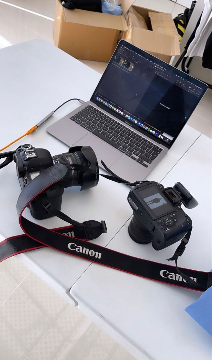 a laptop computer sitting on top of a white table next to two camera's