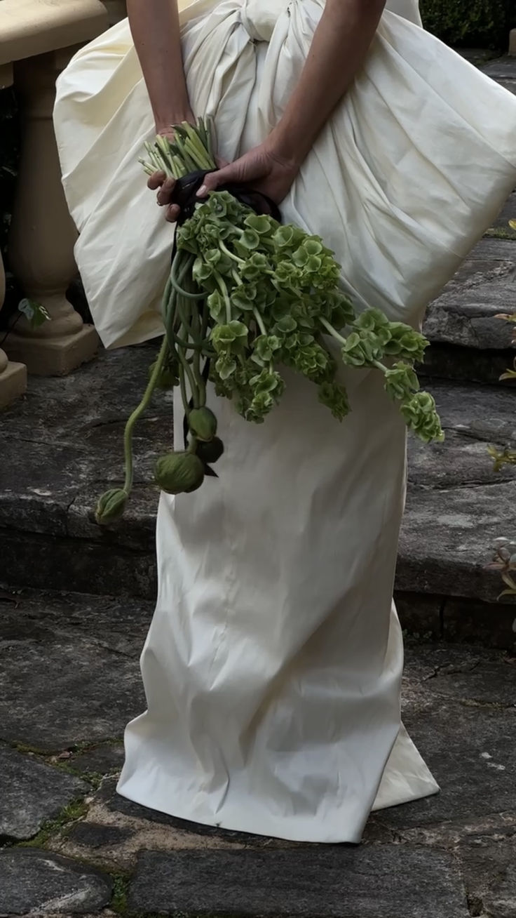 a woman in a white dress holding a bunch of green vegetables on her wedding day