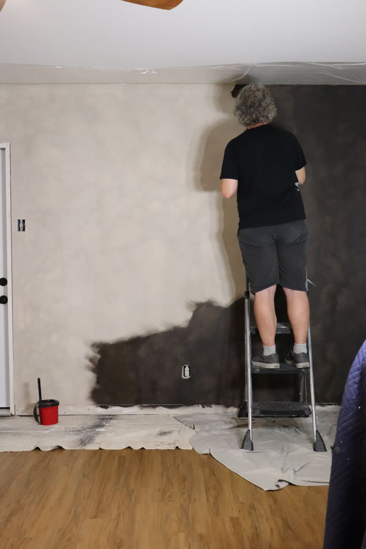 a man on a ladder painting the walls in a room that is being remodeled with wood flooring