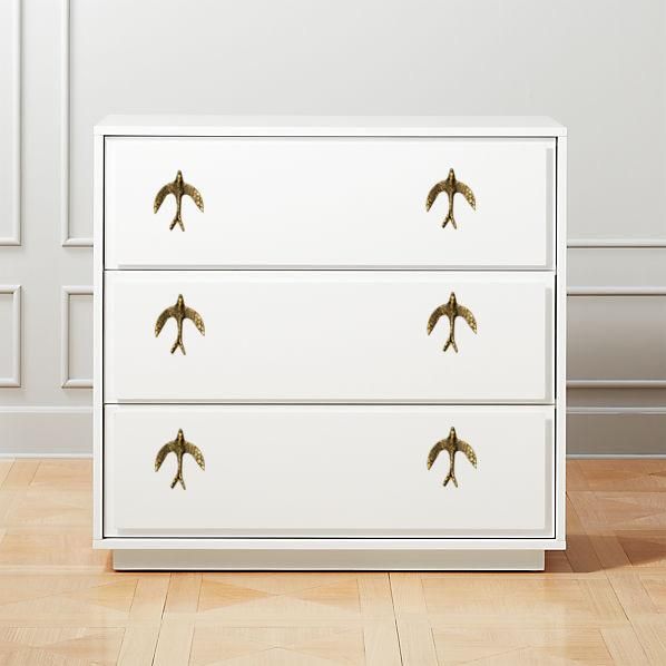 a white chest of drawers with birds painted on the top and bottom, in an empty room