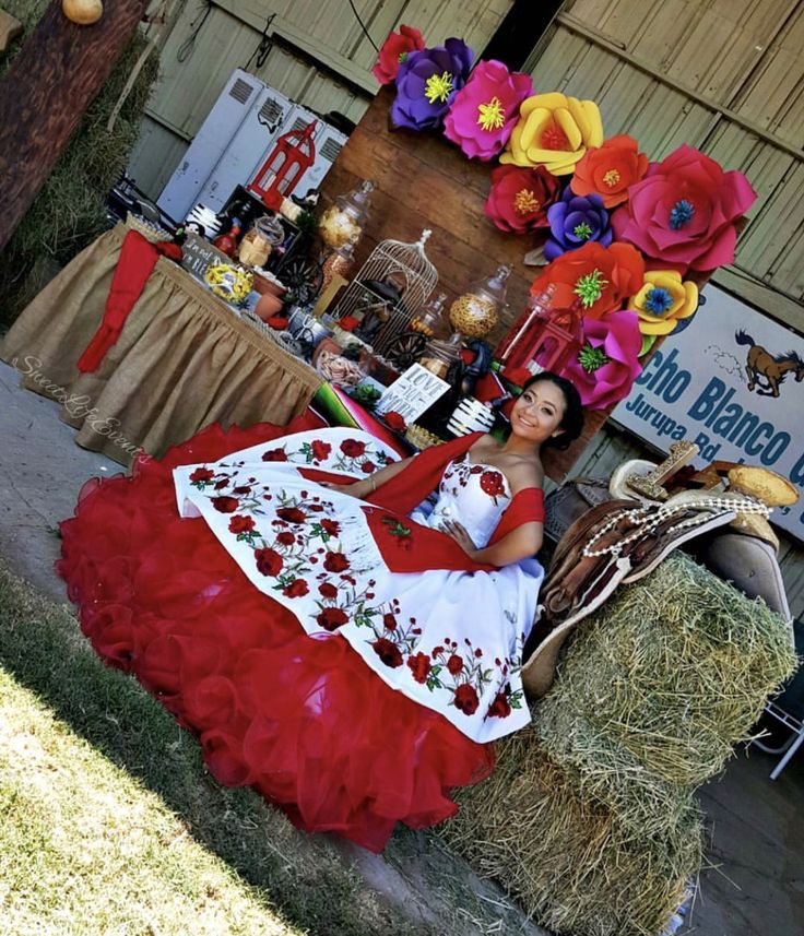 a woman in a red and white dress sitting on hay bales next to flowers