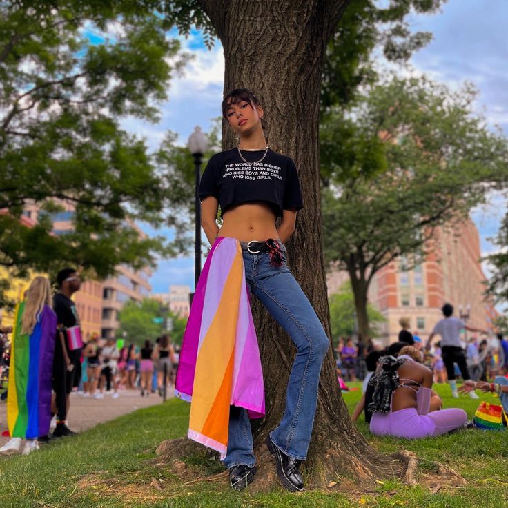 a woman standing in front of a tree wearing a shirt with rainbow stripes on it