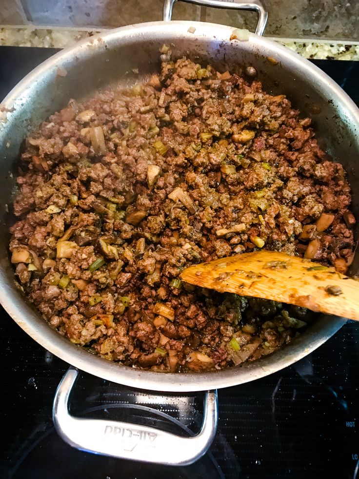 a pan filled with food sitting on top of a stove next to a wooden spoon