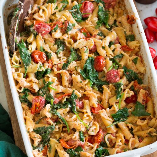 a casserole dish filled with pasta, spinach and tomatoes