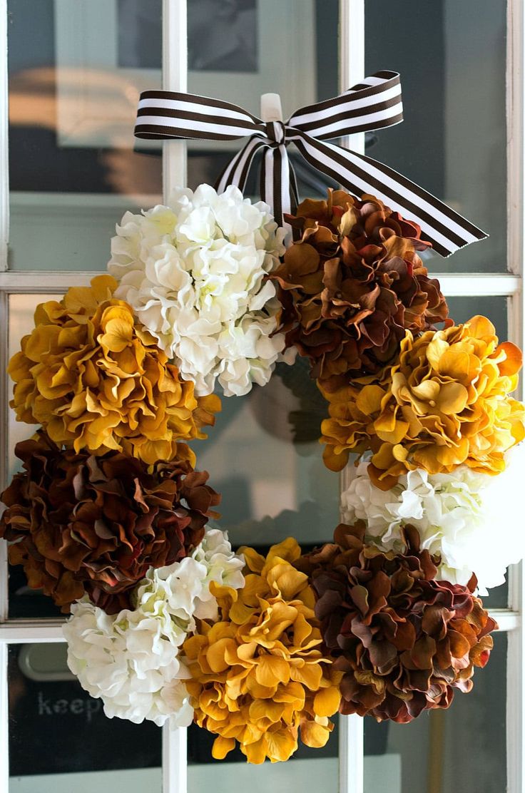 a wreath with white and brown flowers hanging on the front door, decorated with a black ribbon