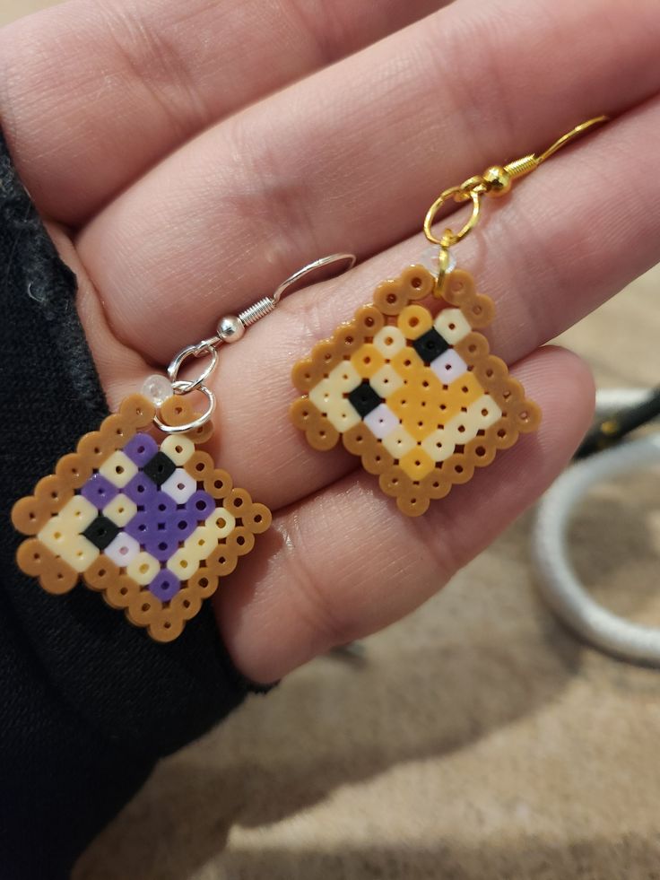 someone is holding two small cross stitch earrings