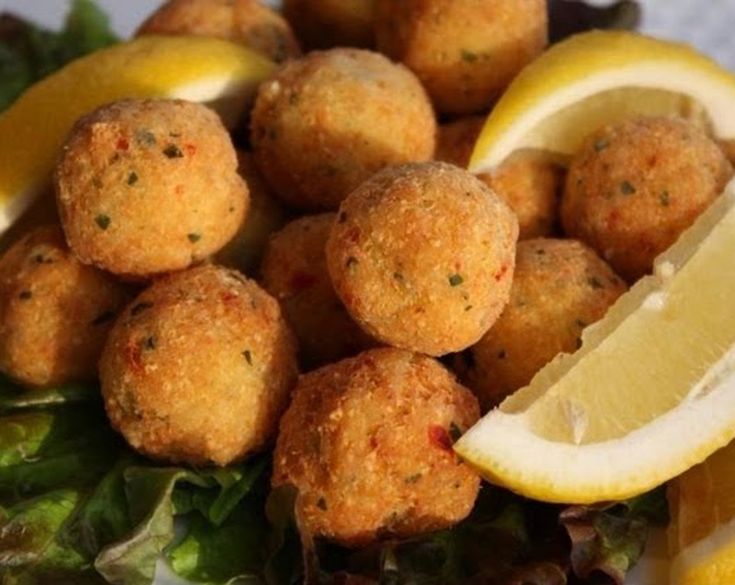 a plate full of food with lemon wedges and meatballs on the side, ready to be eaten