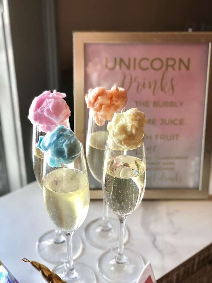 three wine glasses filled with ice cream and candy on a table next to an unicorn sign