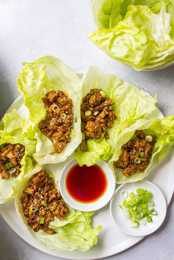 lettuce wraps filled with meat and sauce on a plate next to dipping sauce