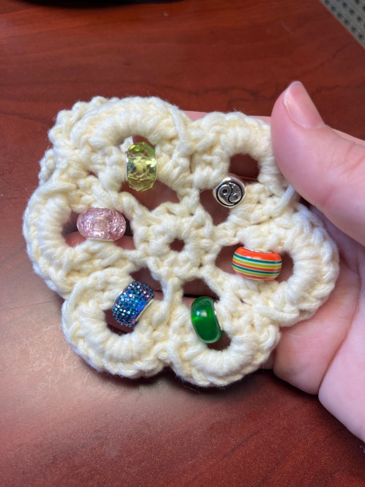 a hand holding a crocheted brooch with lots of different beads on it