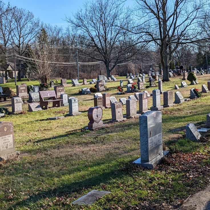 several headstones in a cemetery with trees in the background and grass on the ground