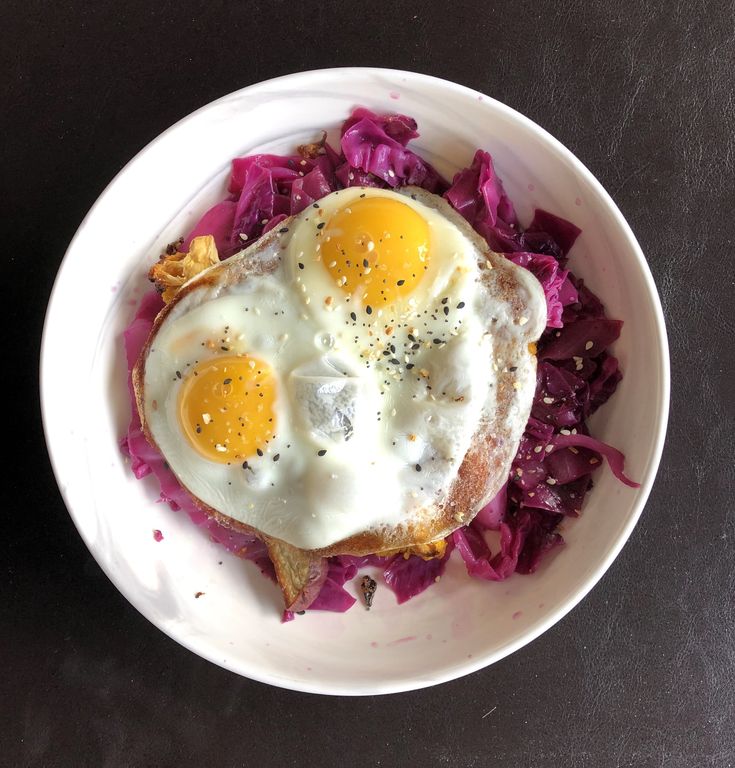 two fried eggs on top of red cabbage in a white bowl