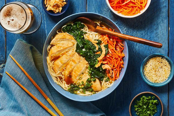 a bowl of noodles, carrots and greens with chopsticks on the side