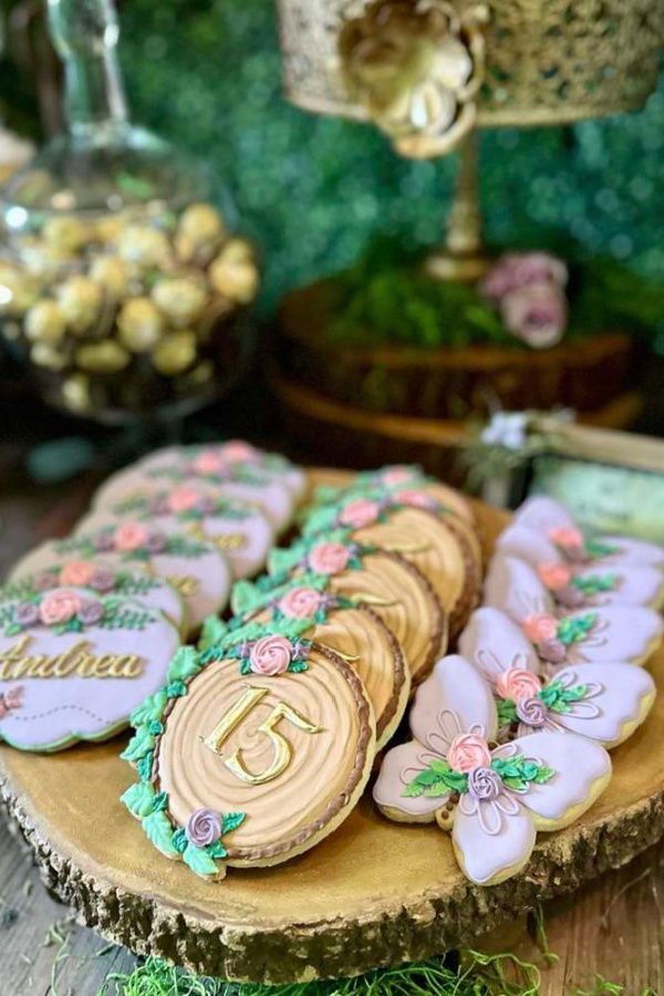 decorated cookies are sitting on top of a tree stump in front of other desserts