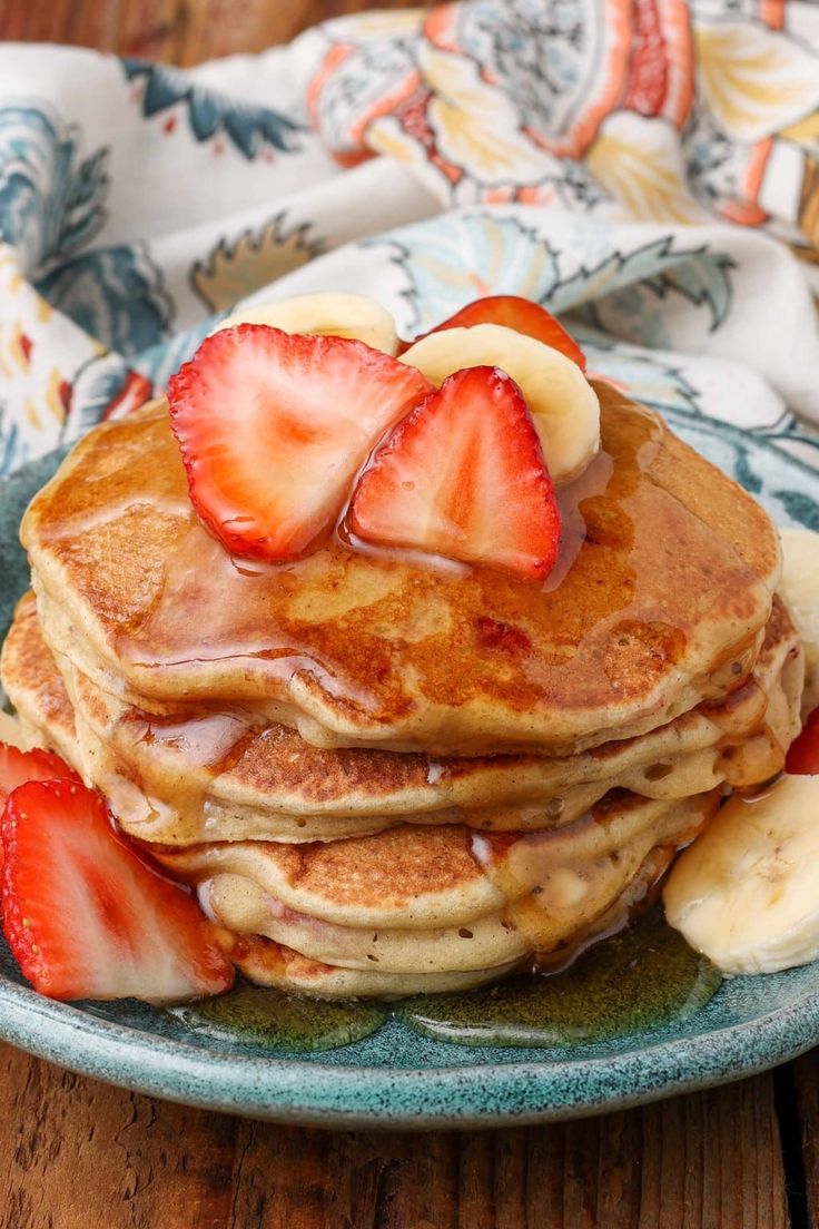 a stack of pancakes topped with sliced bananas and strawberries on a blue plate next to a cup of coffee