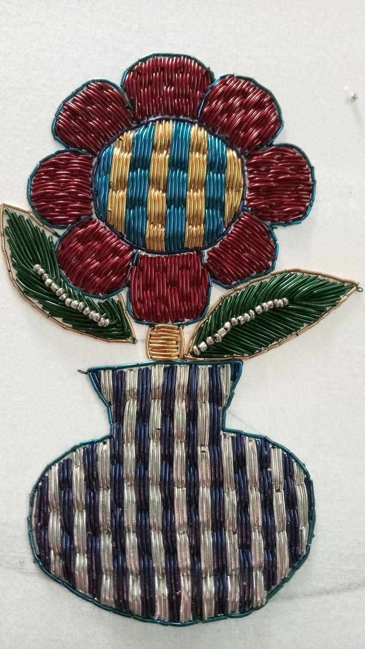 an embroidered flower is sitting on top of a striped vase with green leaves in it