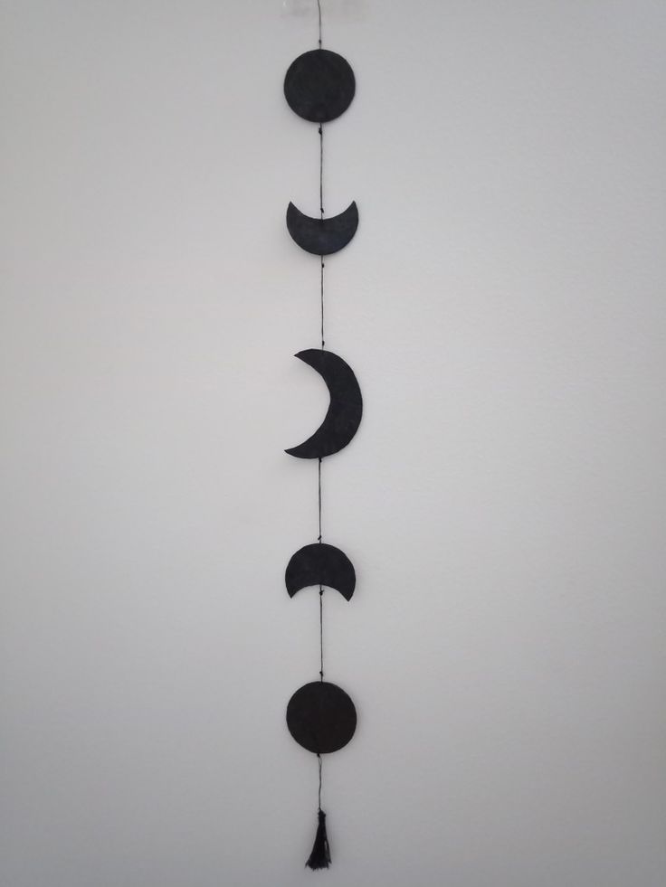 a long metal wall hanging with three moon phases on it's side and a black tassel hanging from the end